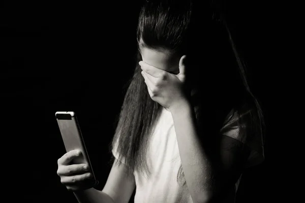 Egy szomorú tini gazdaság mobiltelefon siránkozik, ül az ágyon a hálószobában egy sötét fény a háttérben — Stock Fotó