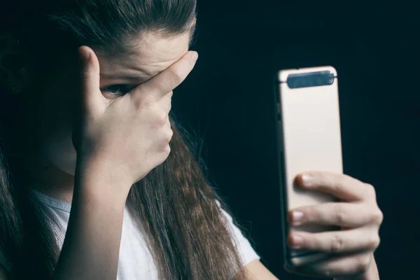 Enda tråkiga tonåring håller en mobiltelefon beklaga sitter på sängen i hennes sovrum med ett mörkt ljus i bakgrunden — Stockfoto