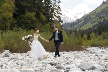 iki sonra düğün kıyafetleri ile bir buket çiçek ve yeşillik bir şelale günbatımı, gelin ve damat ellerinizde