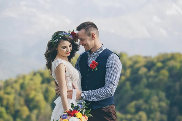 Pareja en traje de novia con un ramo de flores y vegetación está en las manos contra el telón de fondo del campo al atardecer, la novia y el novio —  Fotos de Stock