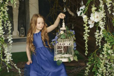 Küçük bir kız ormanda bir hayal ya da fantezi konsepti için büyülü bir kuş kafesi bakarak ışıltı peri kanatları ile oturuyor.