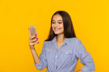 mobil ayakta ve sarı arka plan üzerinde izole gülümseyen mutlu kadın.