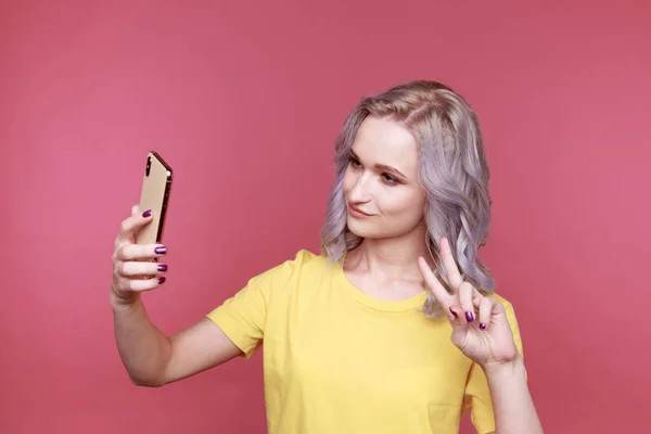 Funny girl in the yellow clothes making self photo on her phone in the pink room. — Stock fotografie