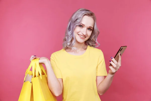 Mooie vrouwelijke persoon met telefoon en boodschappentassen aan de roze muur. — Stockfoto