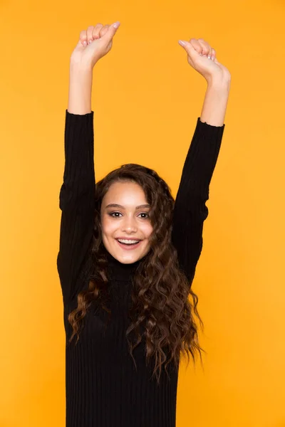 Joyeux sourire jeune femme mettant les mains en l'air dans le studio jaune . — Photo