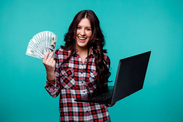 Pretty young woman with money and laptop posing in a studio in a blue background.