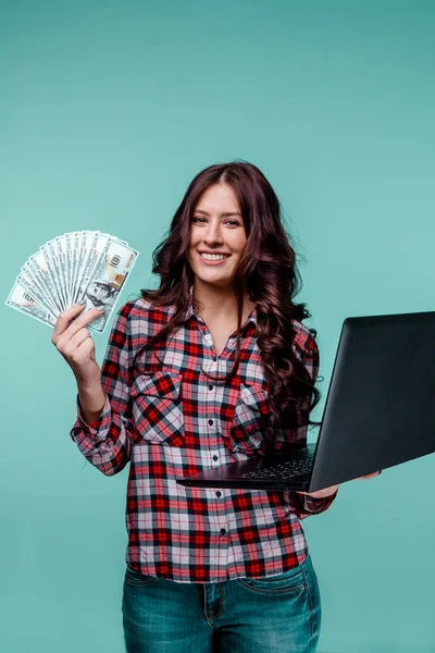 Mooie vrouw holdina geld en laptop op zoek naar de camera geïsoleerd over de blauwe achtergrond. — Stockfoto