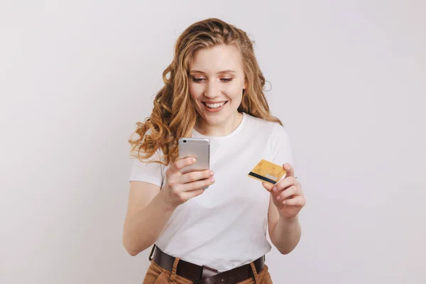 Sonriente modelo guapo posando con su teléfono y tarjeta de crédito y haciendo compras en línea . — Foto de Stock