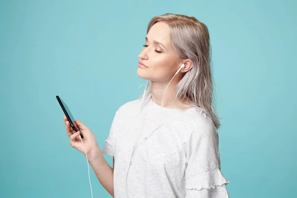 Happy female person with earphones and phone listening to the music in the studio. — Stock Photo, Image