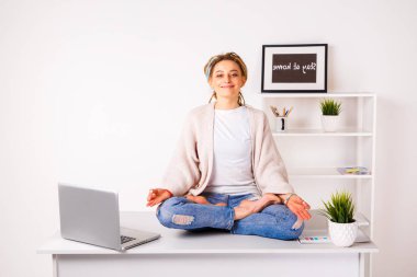 Ofisteki genç kadın laptopuyla masada meditasyon yapıyor..