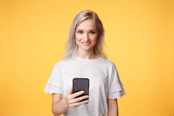 Mladý člověk na žlutém pozadí drží telefon a usmívá se. — Stock fotografie