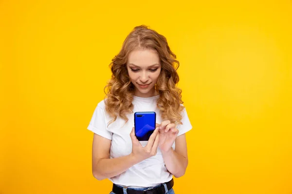 Pretty female holding blue phone isolated in the yellow studio. — Stock fotografie
