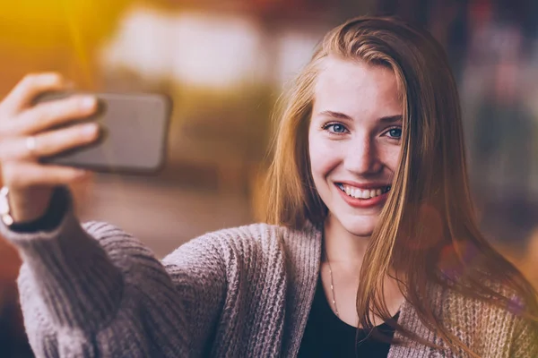 Menina beleza sorrindo e mostrando smartphone com tela vazia para o seu texto no fundo do café. Close-up foto de menina sorridente atraente em pé no fundo cinza e segurando — Fotografia de Stock