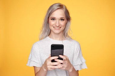 Sarı stüdyoda siyah telefon kullanan sevimli sarışın kadın..