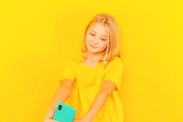Niña sonriente que muestra la pantalla azul del nuevo teléfono móvil popular sobre fondo amarillo claro . —  Fotos de Stock