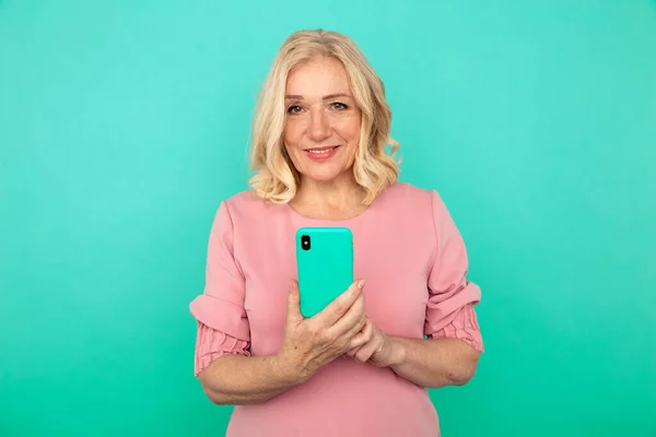 Happy mature woman with mobile isolated over the blue background.