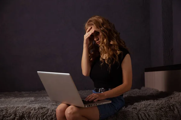Depresyonda olan ciddi bir kadın yatakta oturuyor ve dizüstü bilgisayarla çalışıyor.. — Stok fotoğraf