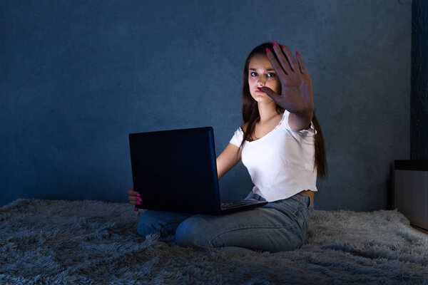 Scared teen girl with stop sign infront of the laptop sitting on the bed.
