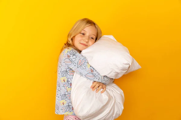 Urocza dziewczynka patrząc w aparat i przytulając tło poduszki żółtej ściany — Zdjęcie stockowe