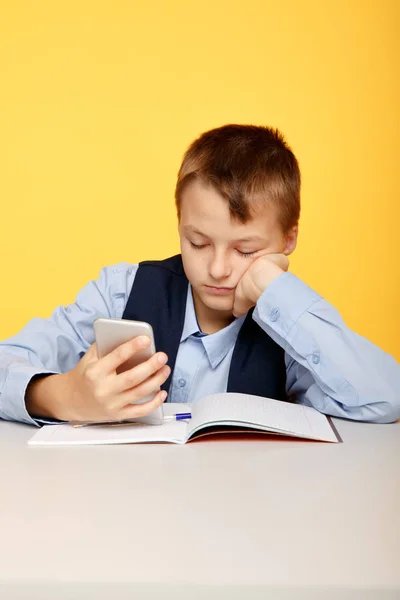 Verveelde jongen pupil kijken telefoon bij de les in de gele klas. — Stockfoto
