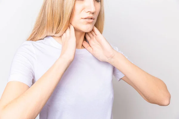 Weibchen checken Schilddrüse selbst. Großaufnahme einer Frau in weißem T-Shirt, die den Hals mit rotem Fleck berührt. Schilddrüsenerkrankungen umfassen Kropf, Schilddrüsenüberfunktion, Schilddrüsenunterfunktion, Tumor oder Krebs. Gesundheitsversorgung. — Stockfoto