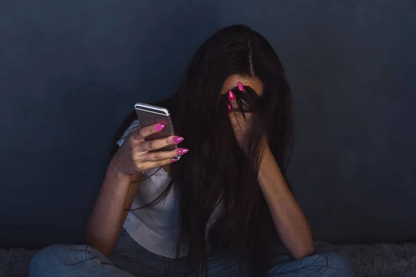 En deprimerad ung kvinna stängde ansiktet för hand och höll telefonen. Dåligt online-koncept. — Stockfoto