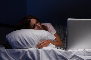 Yatakta dizüstü bilgisayarlı uyuyan genç bir internet bağımlısı..