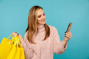 Sarı çantaları ve mavi arka planda izole edilmiş telefonu olan güzel bir genç kadın. Satış konsepti.
