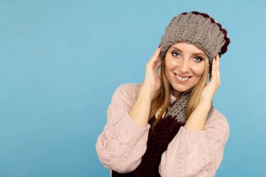 Mavi arka planda izole edilmiş, kış şapkalı, gülümseyen güzel bir kadının yakın plan portresi..