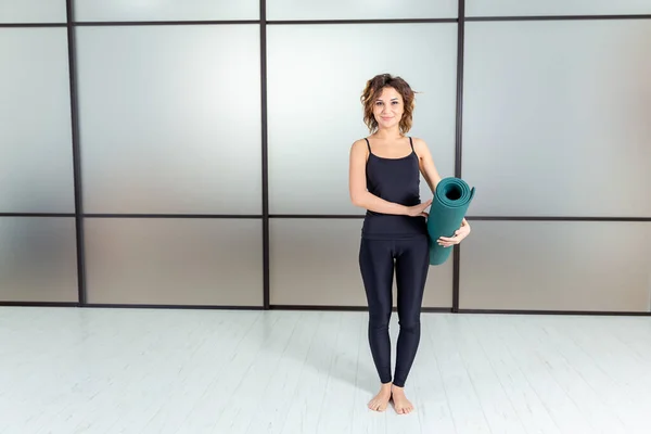 Yoga drinnen. junge Frau in Sportkleidung macht sich bereit für Gymnastik und Yoga mit grüner Matte. — Stockfoto