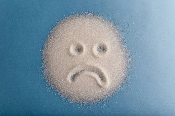 Sad sugar face on the blue background. Bad food concept. — Stock Photo, Image