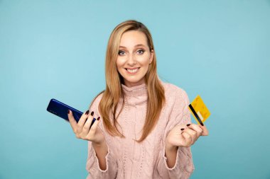 Mavi stüdyoda kredi kartı ve cep telefonu olan mutlu bir kadın var..