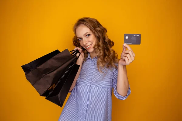 Nákupní prodej. Krásná žena s taškami a kreditní kartou ve žlutém studiu. — Stock fotografie