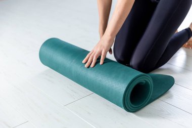 Closeup picture of yoga green mat. Woman is getting ready for exercises indoor.