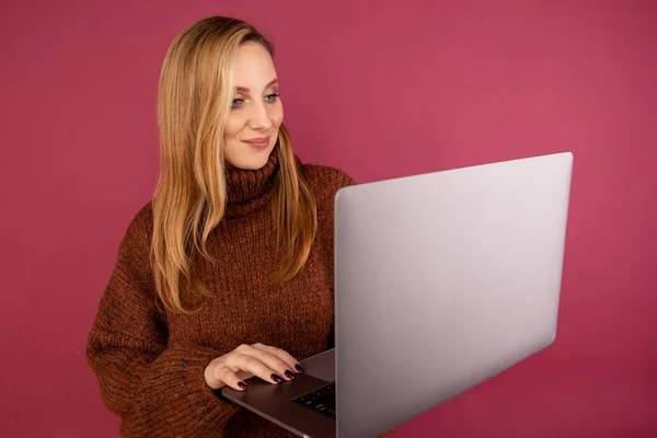 Happy woman with laptop isolated in the pink studio.