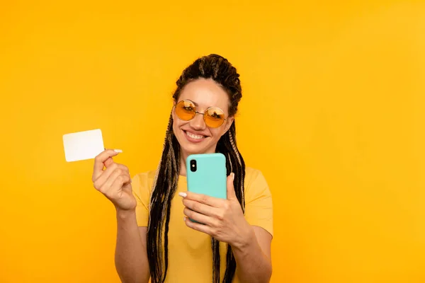 Happy woman in the yellow T-shirt holding credit card with mobile.