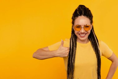 Mutlu gülümseyen kadın sarı arka planda başparmağını kaldırıyor..