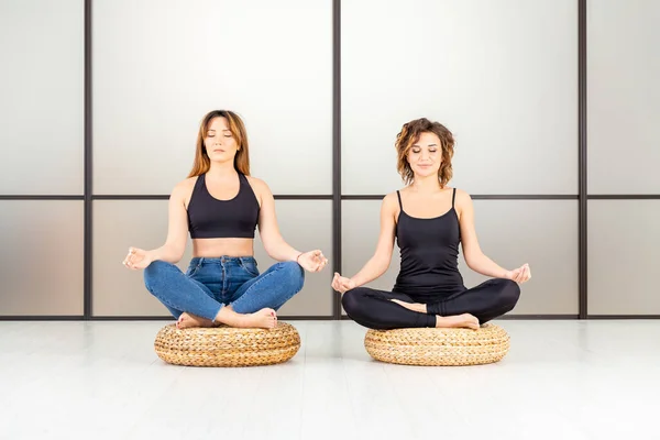 Meditating women sitting in the lotus pose with closed eyes in the white room. Its yoga time.