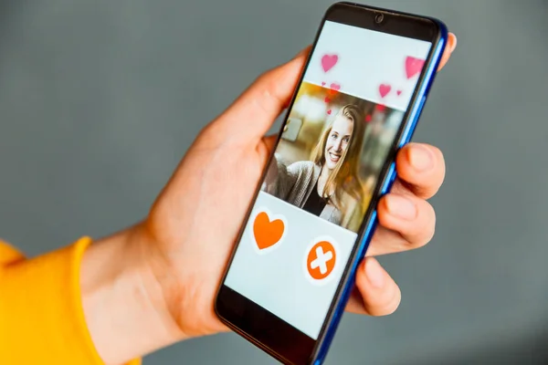 Online dating app in smartphone. Man looking at photo of beautiful woman. Person swiping and liking profiles on relationship site or application. Single guy searching for love partner. Mockup website.