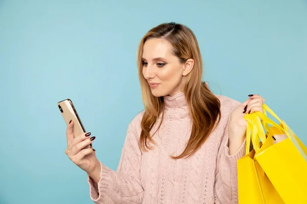 Mladá usměvavá žena s úsměvem a pomocí telefonu drží žluté nákupní tašky izolované. — Stock fotografie