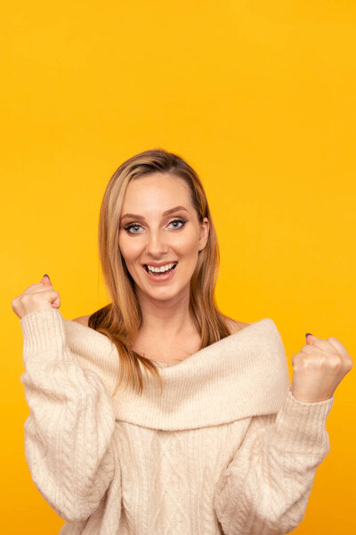 Portrait of smiling woman winner in the sweater posing on the yellow wall.
