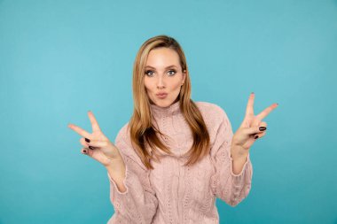 Şık bir bayan model, eğleniyor ve mavi stüdyoda barış işareti gösteriyor..