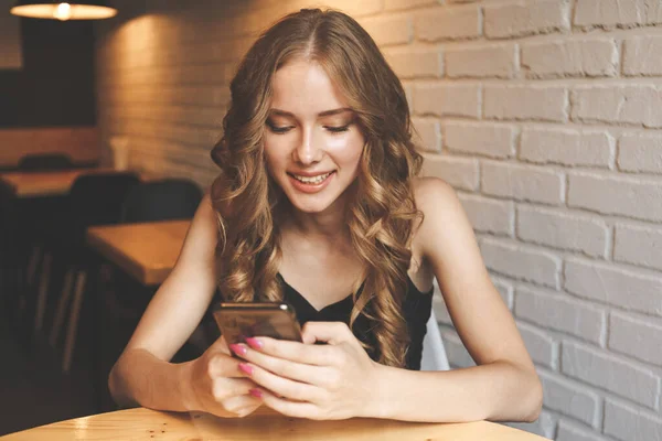 Ritratto di una donna bionda carina leggere qualcosa sul suo smartphone mentre seduto nel caffè moderno — Foto Stock