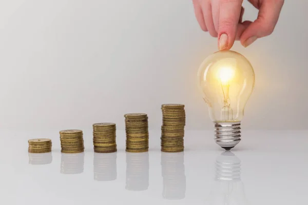 Hand holding a light bulb with coins stack. Creative ideas for saving money concept. Money management for the future