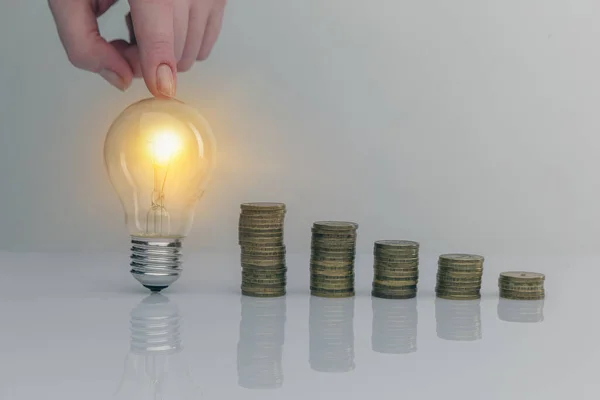 Hand holding a light bulb with coins stack. Creative ideas for saving money concept. Money management for the future