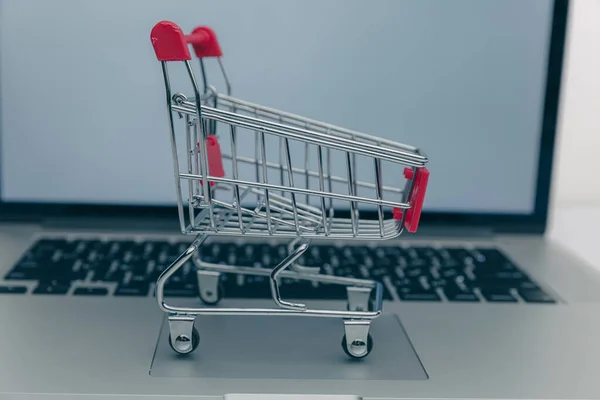Laptop und kleiner Einkaufswagen auf weißem Hintergrund. Einkaufskonzept im Internet — Stockfoto