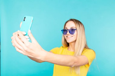 Parlak tişörtlü güzel bir sarışının yakın plan portresi. Mutlu genç bayan özçekim yapar ve gülümser.