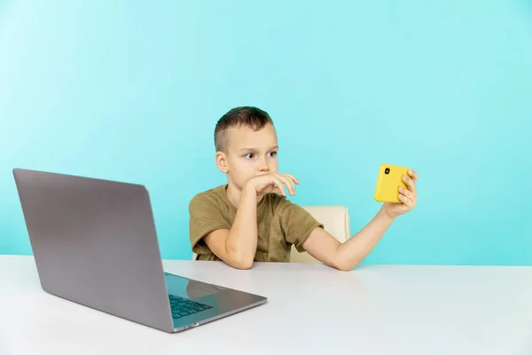Gelukkige jongen op afstand onderwijs praten iemand telefoon en met behulp van de computer om te studeren. — Stockfoto
