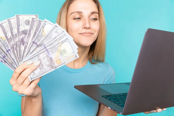 Portret zadowolonej dziewczyny trzymającej banknoty z laptopem na niebieskim tle. Portret młodej kobiety z banknotami i laptopem w ręku — Zdjęcie stockowe