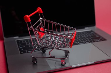 İnternetten alışveriş konsepti. Laptop ve pembe arka planda küçük sepet..